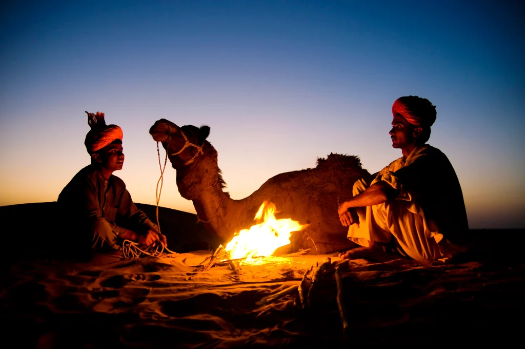 Indian men resting near a campfire with their camel
